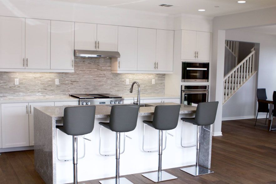 Modern white kitchen with island, four gray bar stools, stainless appliances, and wood floors