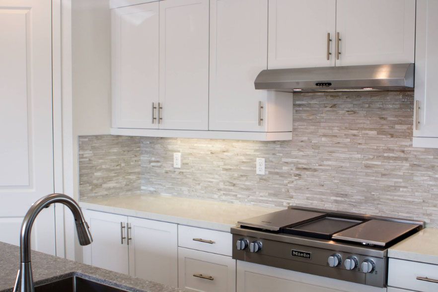 Bright modern kitchen with white cabinets, tile backsplash, sink, and stainless steel stove under a range hood