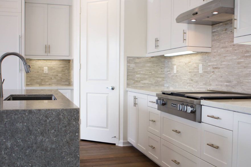 Bright modern kitchen with white cabinets, gray backsplash, island sink, and stainless steel range