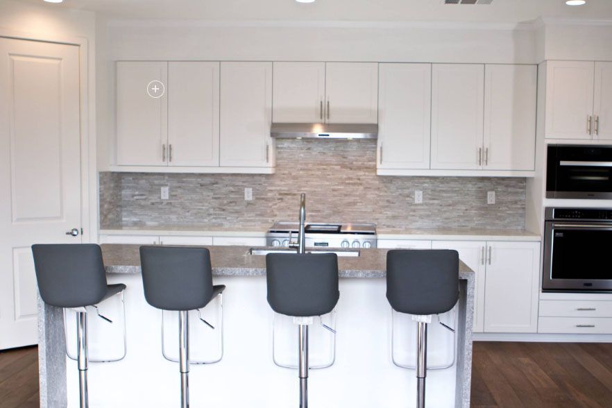 Modern white kitchen with island, four gray stools, stainless steel appliances, and tiled backsplash