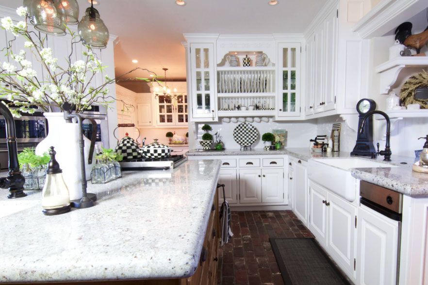 Bright white kitchen with marble island, white cabinets, dark wood floors, and green floral decor