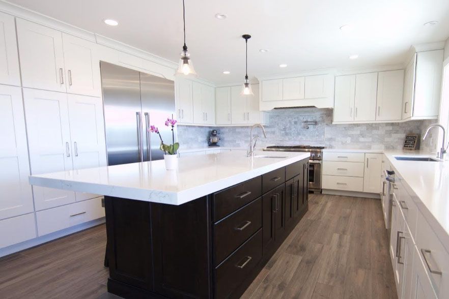 Bright modern kitchen with white cabinets, stainless steel appliances, dark island, and wood-look flooring