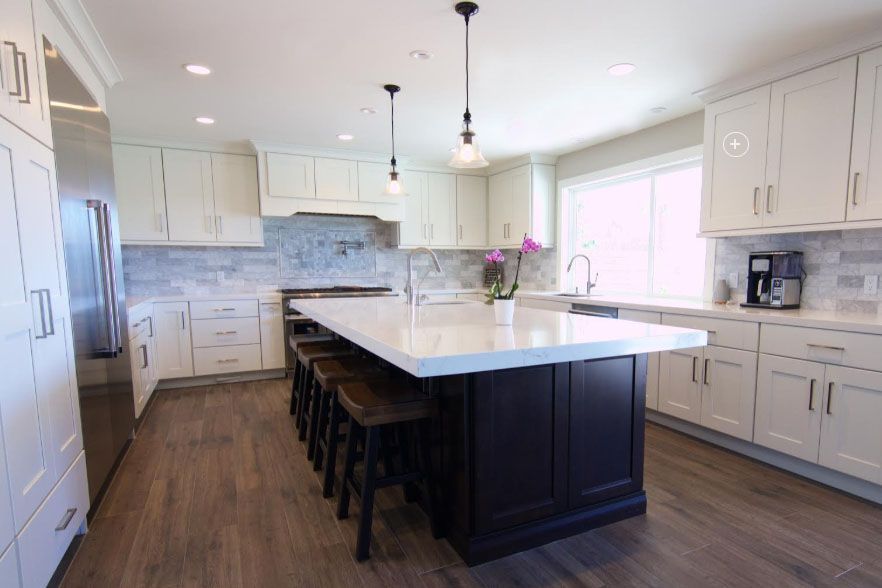 Bright modern kitchen with white cabinets, large island, pendant lights, and dark wood floors