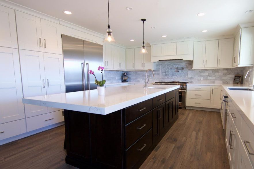 Modern white kitchen with dark island, stainless appliances, and pendant lights