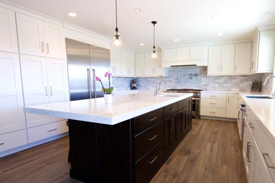 Bright modern kitchen with white cabinets, dark island, stainless appliances, and wood floors
