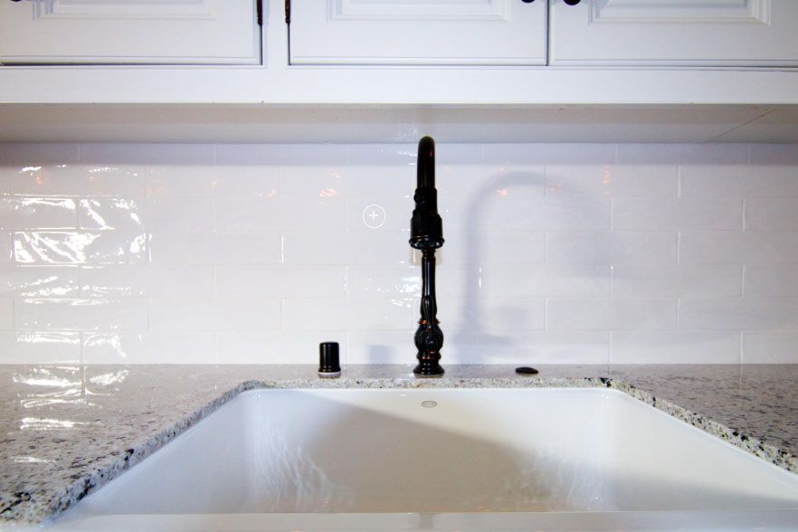 Kitchen sink with black faucet against a white tile backsplash and granite countertop.