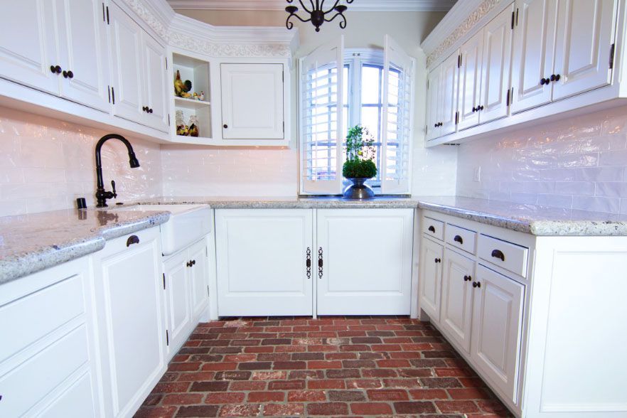 Bright white kitchen with white cabinets, granite counters, and a brick floor under a window.