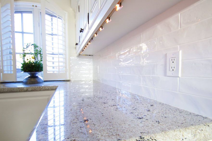 Bright kitchen with white subway tile backsplash, speckled countertop, and window seat with potted plant.