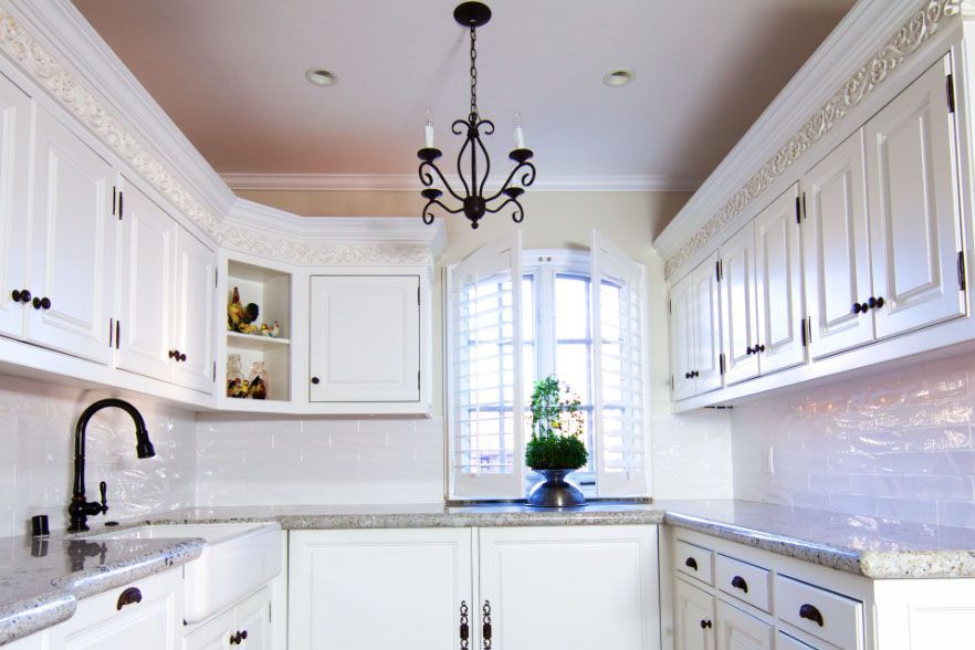 Bright white kitchen with cabinets, black faucet, marble counters, and window above the sink