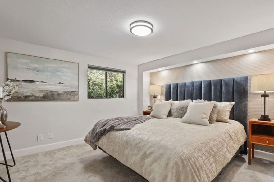 Bright bedroom with a large bed, gray carpet, and a window with dark curtains