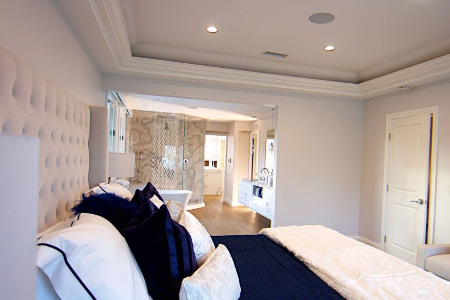 Bright bedroom with tufted headboard, navy bedding, and a view into a marble bathroom and hallway.