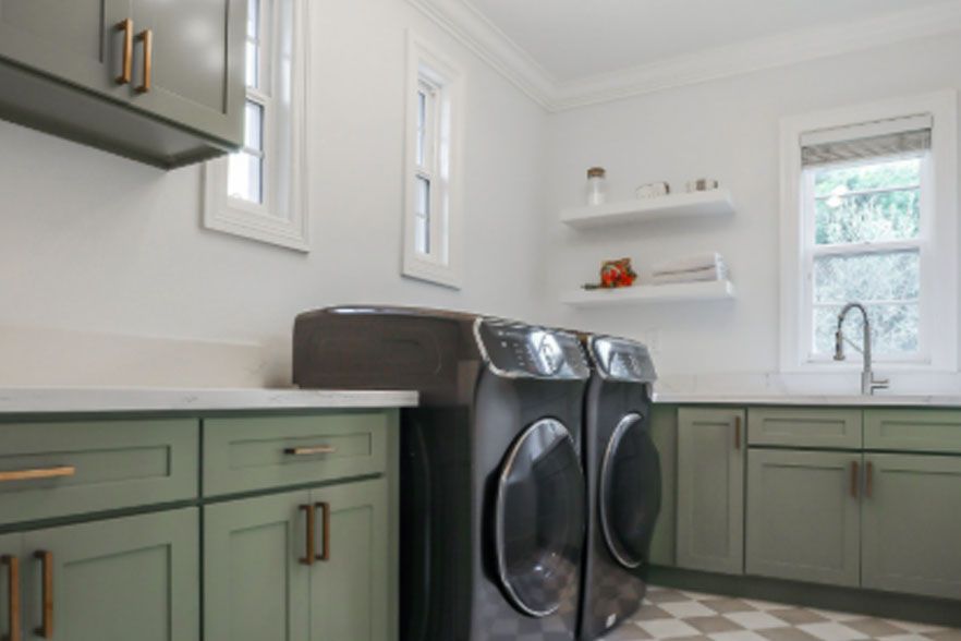 Laundry room with green cabinets, black washer and dryer, white walls, and checkered tile floor