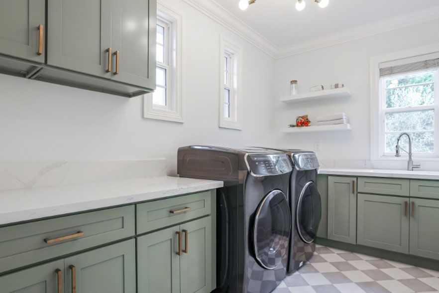 Laundry room with sage cabinets, white countertops, and a washer and dryer by a window