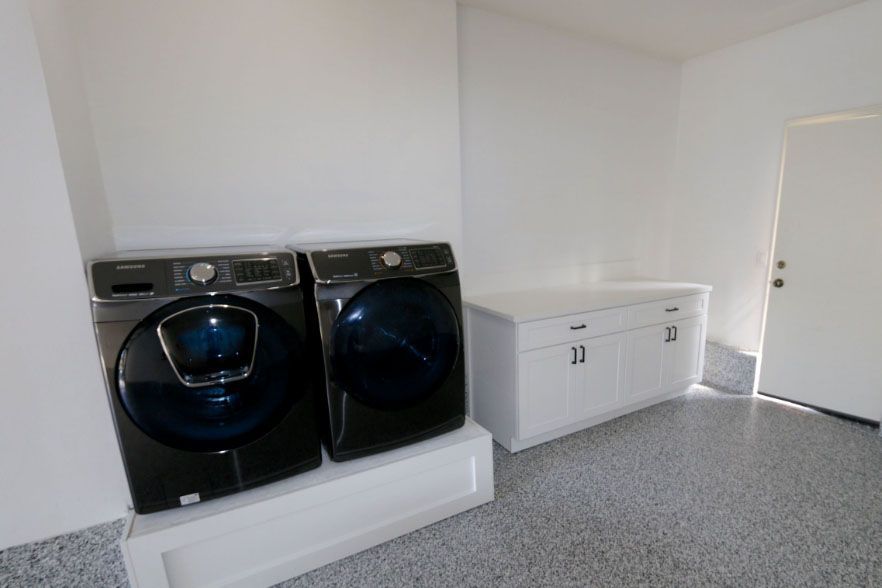 Laundry room with black washer and dryer beside white cabinets on gray carpet