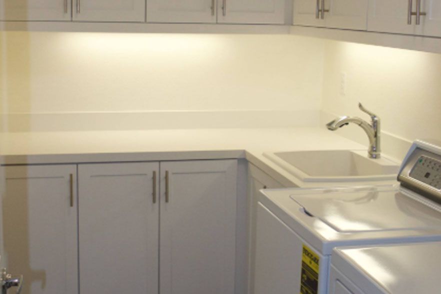 Modern kitchen with white cabinets, sink, faucet, and countertop near a window.