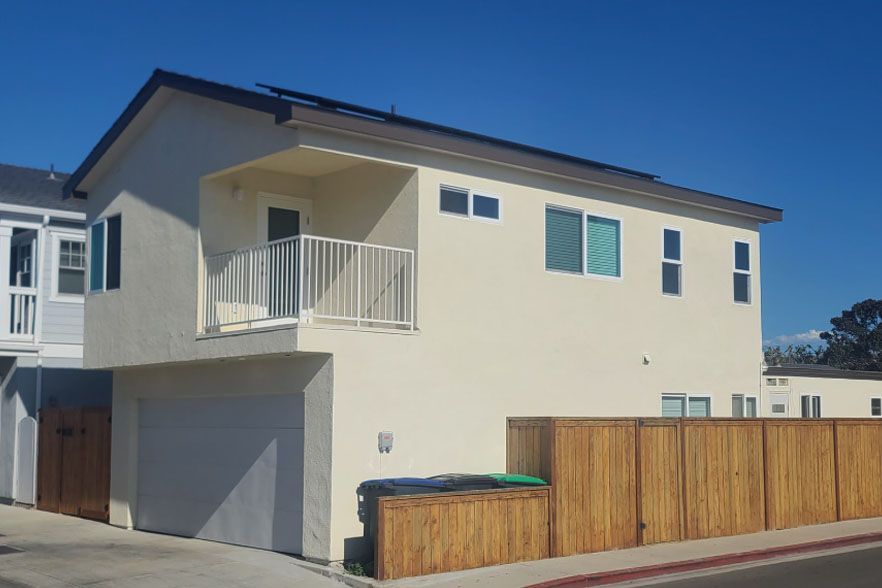 Modern beige two-story house with garage, balcony, and wood fence under a clear blue sky