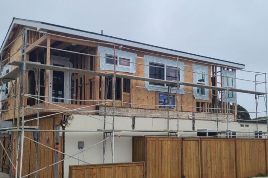 Two-story house under construction with scaffolding and a wooden fence in front