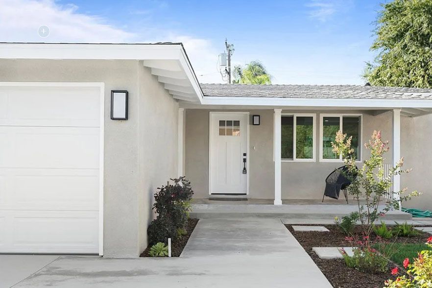 Modern single-story house exterior with white garage, front porch, and landscaped entryway