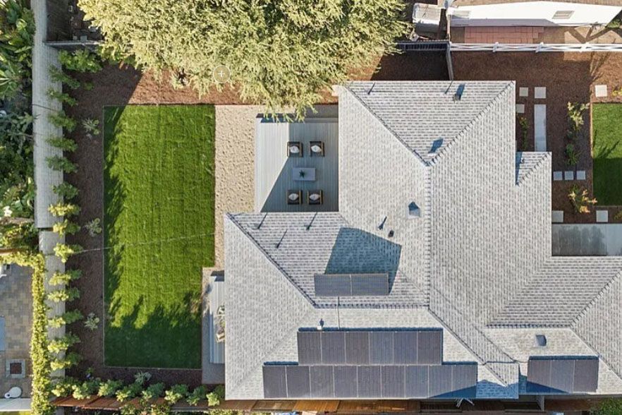 Aerial view of a house roof with solar panels, backyard lawn, and trees.