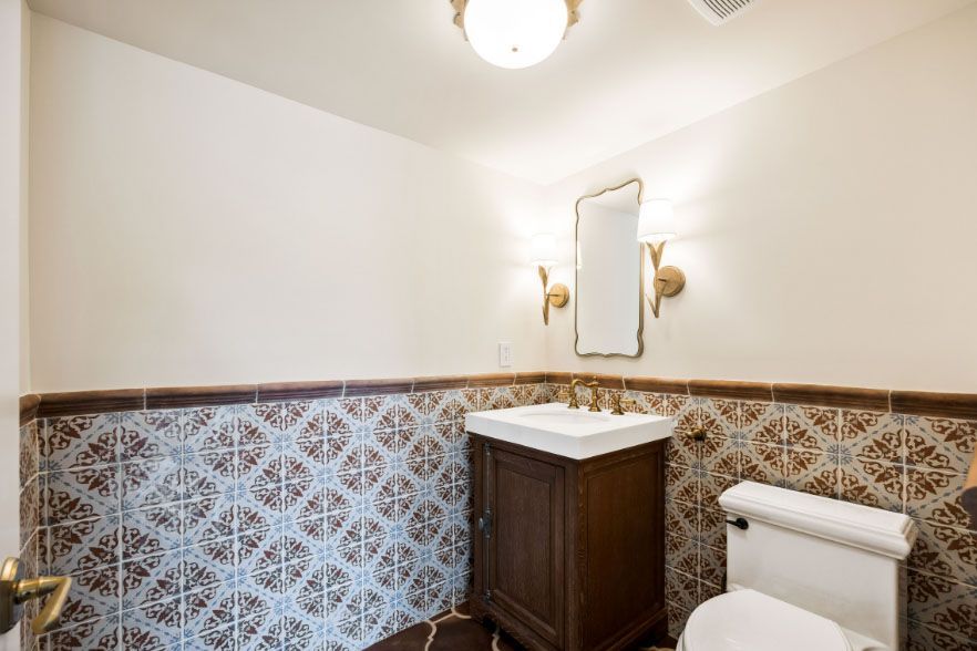 Small bathroom with patterned tile wainscoting, pedestal sink, mirror, and toilet