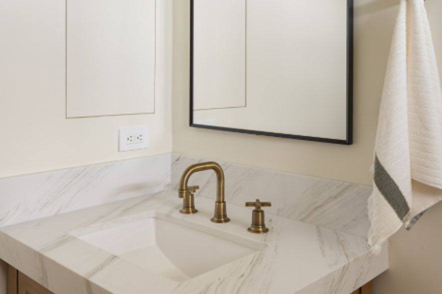 White marble bathroom vanity with brass faucet, mirror, and towel beside sink.