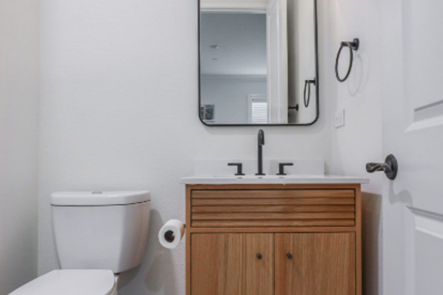 Small white bathroom with toilet, wood vanity, mirror, and towel ring