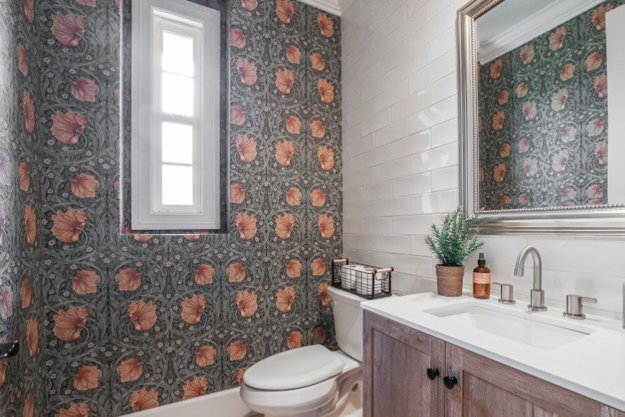 Modern bathroom with floral wallpaper, white tile shower, vanity sink, and toilet