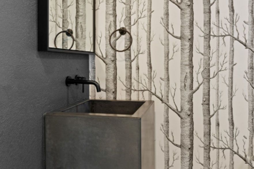 Rustic metal sink with black faucet against birch-patterned wallpaper and gray wall