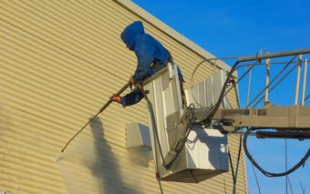 A man is cleaning a building with a high pressure washer.