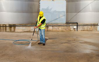 A man is using a high pressure washer to clean the ground.