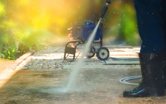 A person is using a high pressure washer to clean a sidewalk.