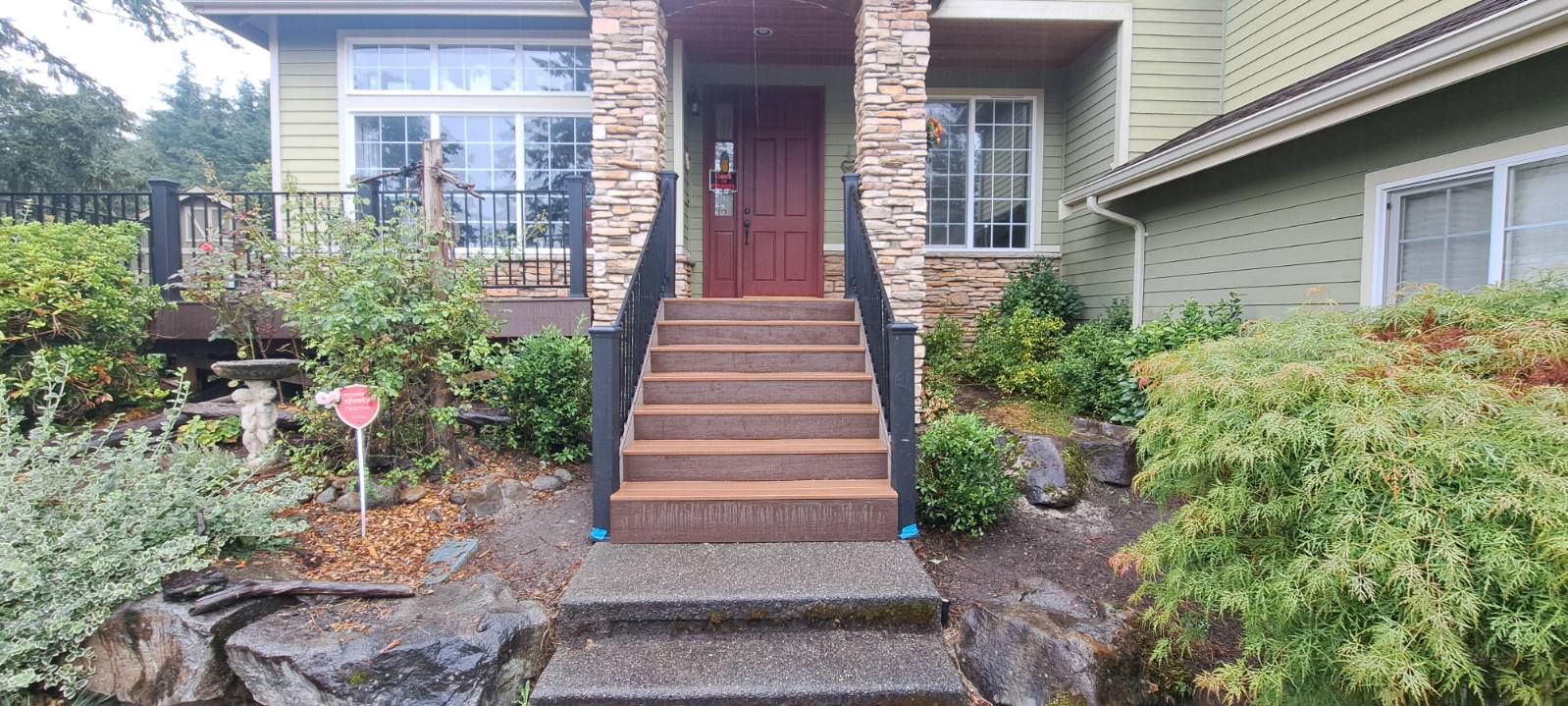Front steps to a brick house with a red door, surrounded by shrubs and a landscaped garden.