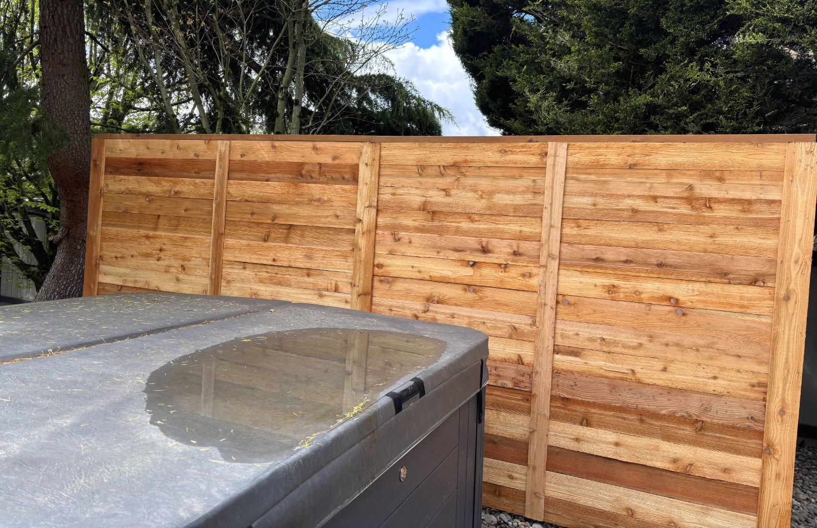 Wooden privacy fence behind a gray hot tub cover under a cloudy sky