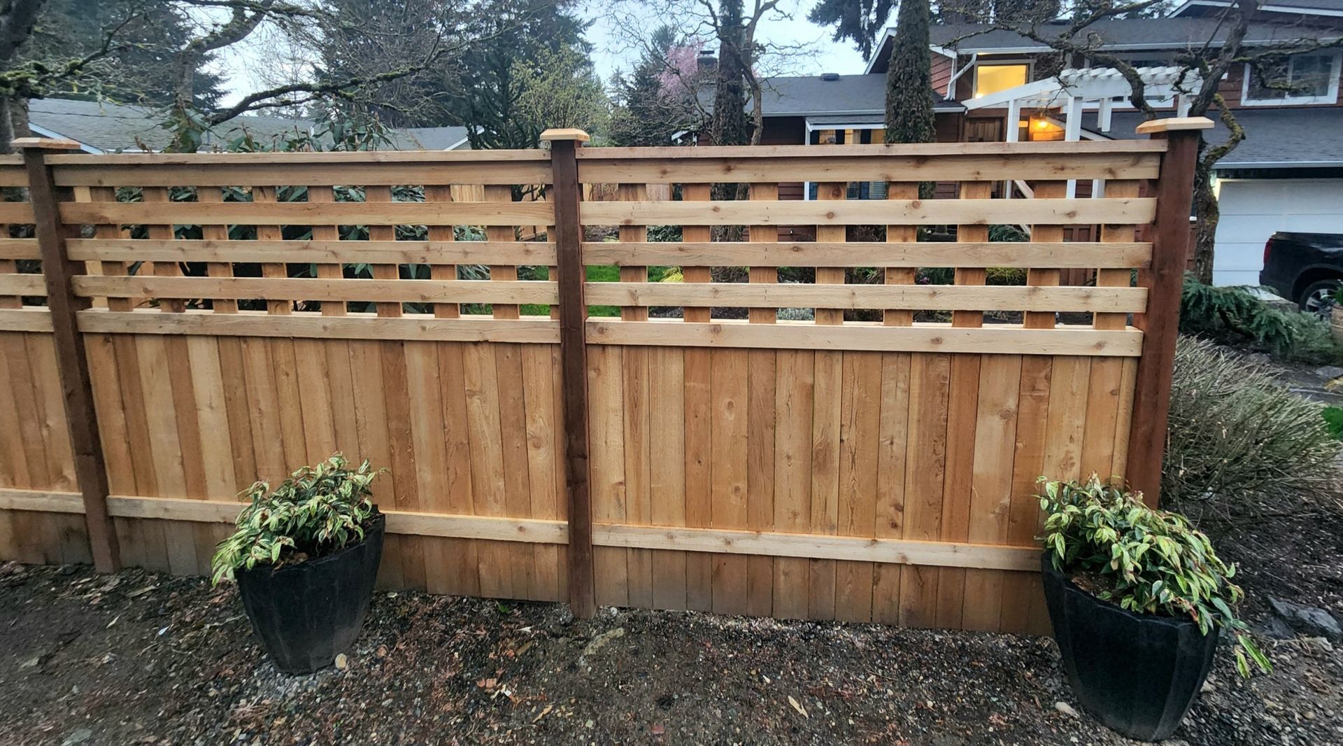 Wooden privacy fence with lattice top and two black planters in a front yard