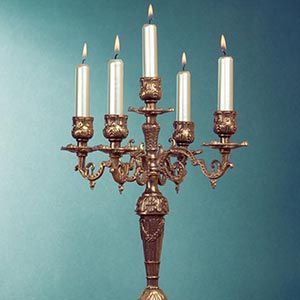 Ornate bronze candelabra with five lit white candles on a teal background
