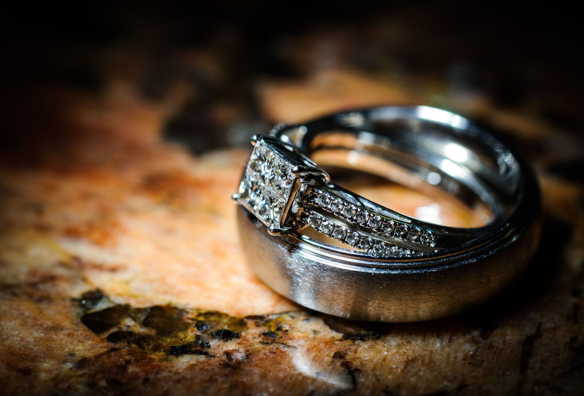 Two silver rings with a diamond setting on a mottled stone surface, softly lit