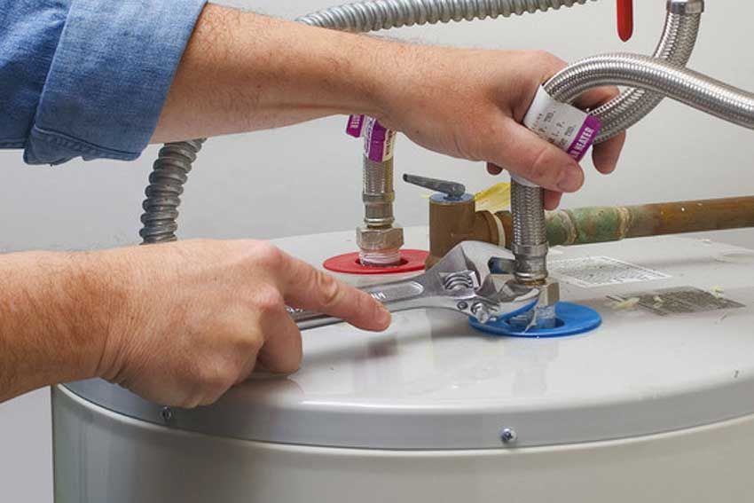 A person is fixing a water heater with a wrench.