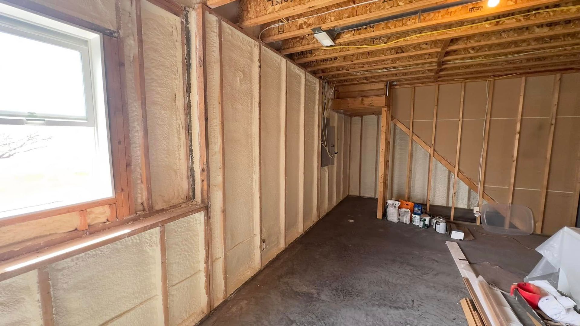 Unfinished room with exposed insulation, window, and construction materials on the floor.