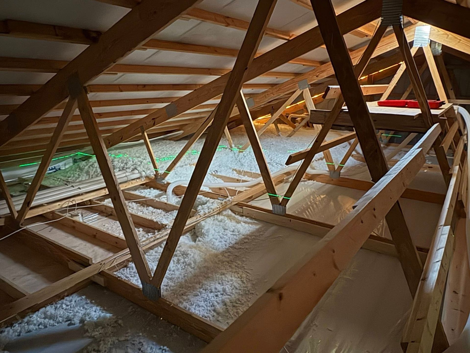 Inside a wooden attic, roof trusses and beams are covered with a light dusting of snow.