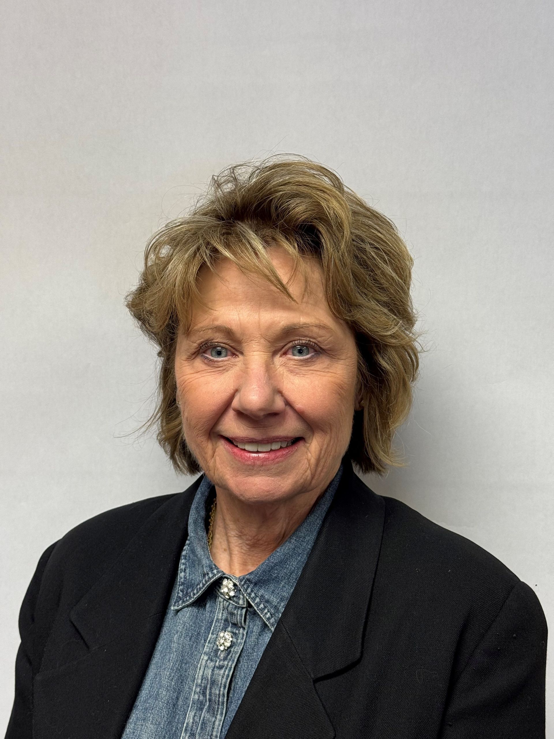 A woman wearing a black jacket and a blue shirt is smiling for the camera.