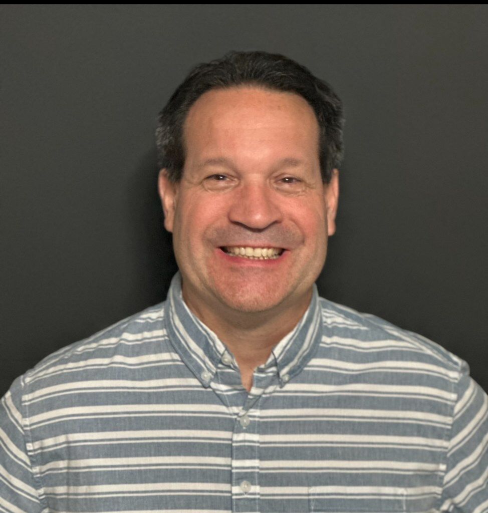 A man wearing a striped shirt is smiling for the camera