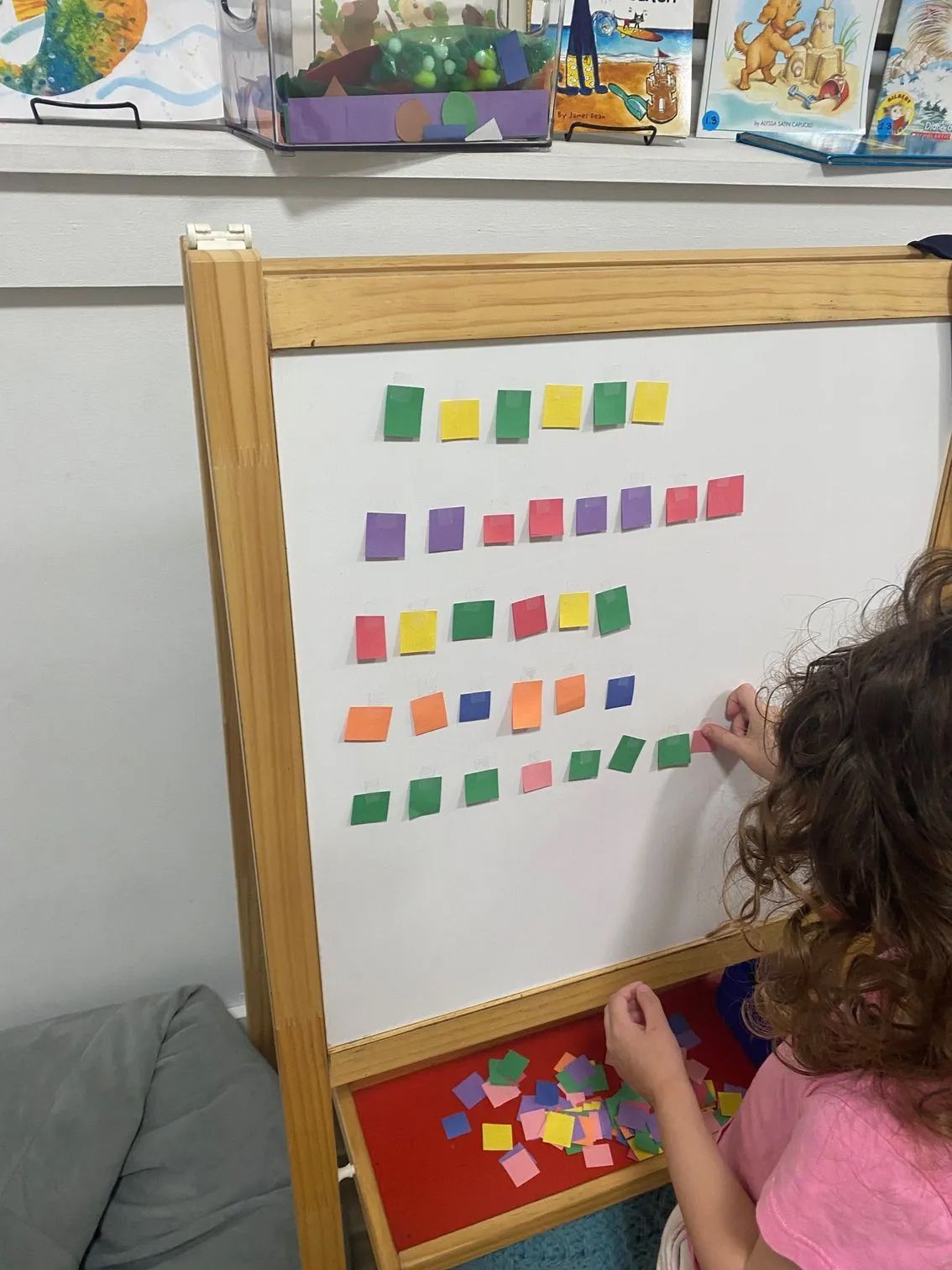A child arranging colorful square magnets on a whiteboard easel.