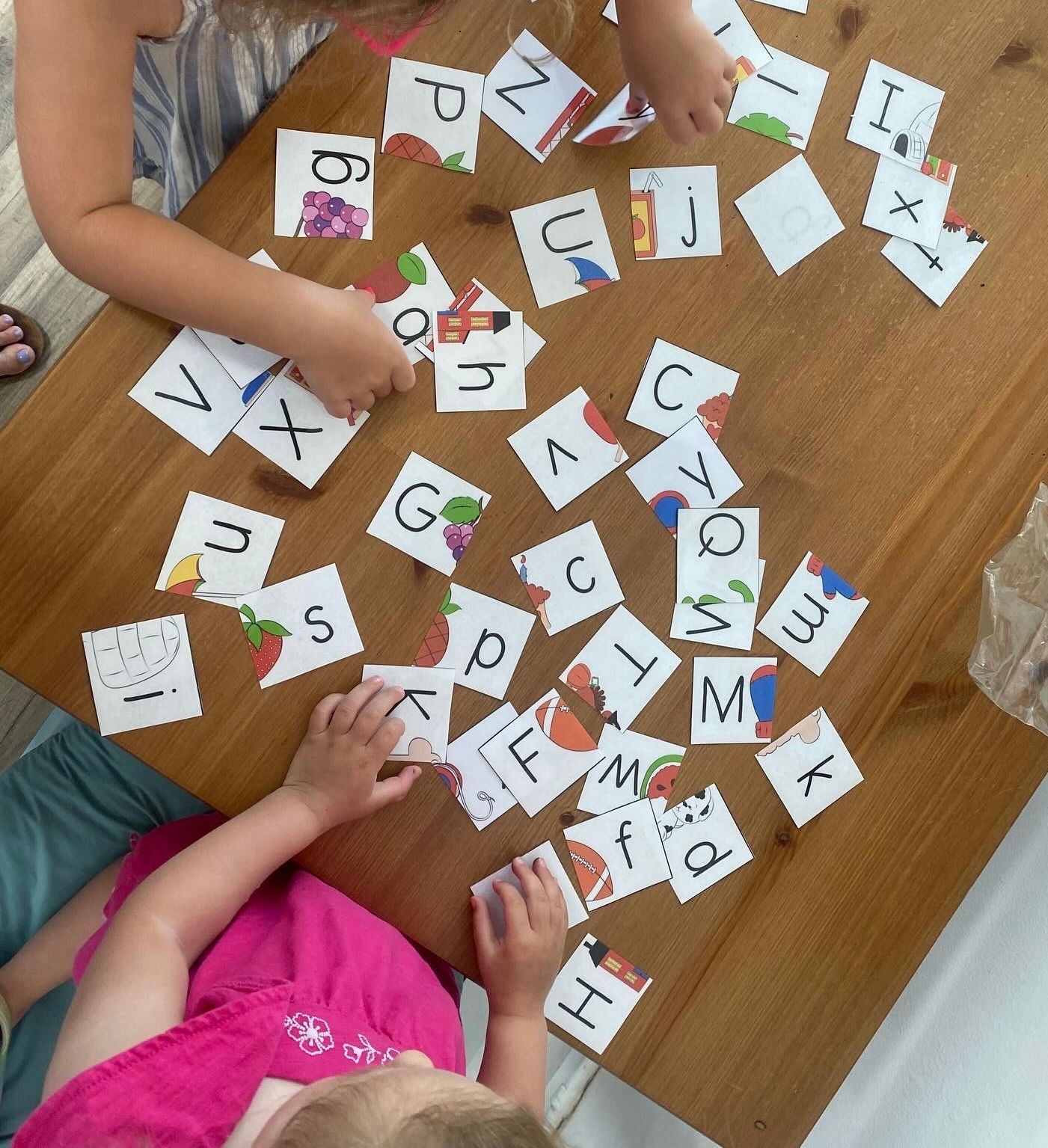Two children playing a letter matching game on a wooden table.
