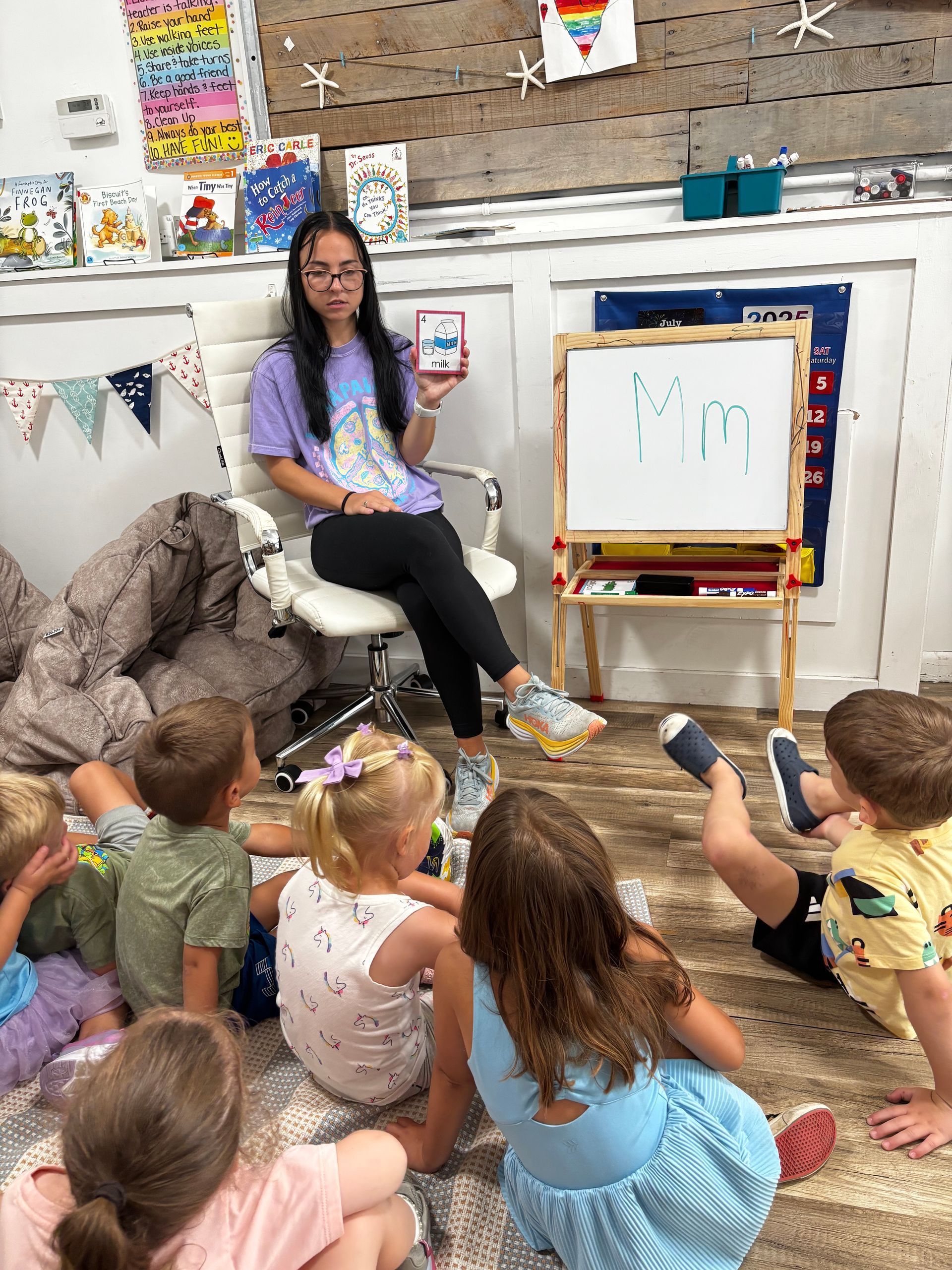 Teacher showing flashcard to children, sitting on the floor in a classroom.