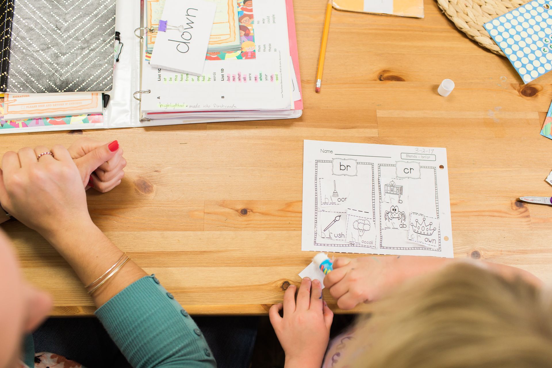 Hands of a person and child working on a drawing together on a wooden table.