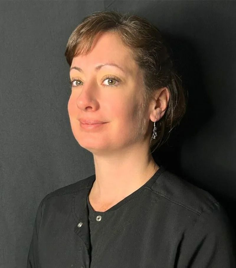 Portrait of a person in a black shirt against a dark background, facing left with a slight smile