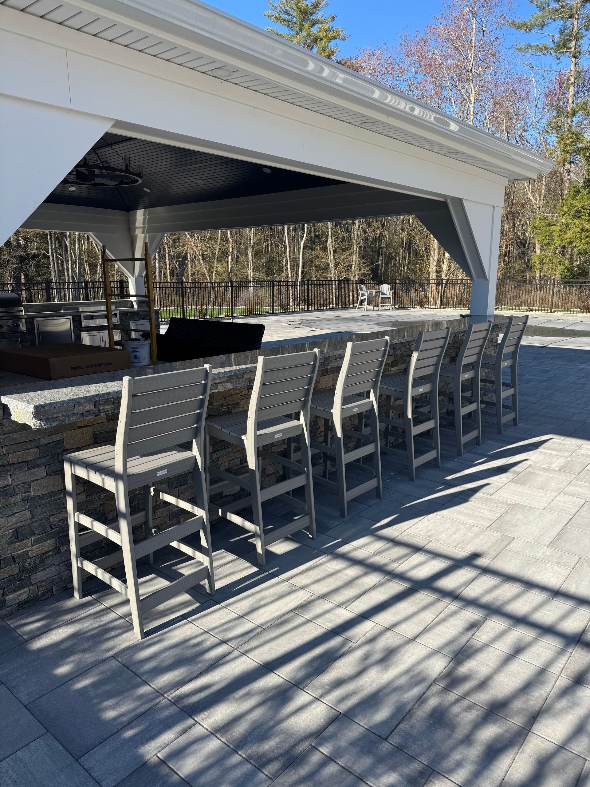 Outdoor covered bar with stone counter and rows of gray chairs on a sunny patio
