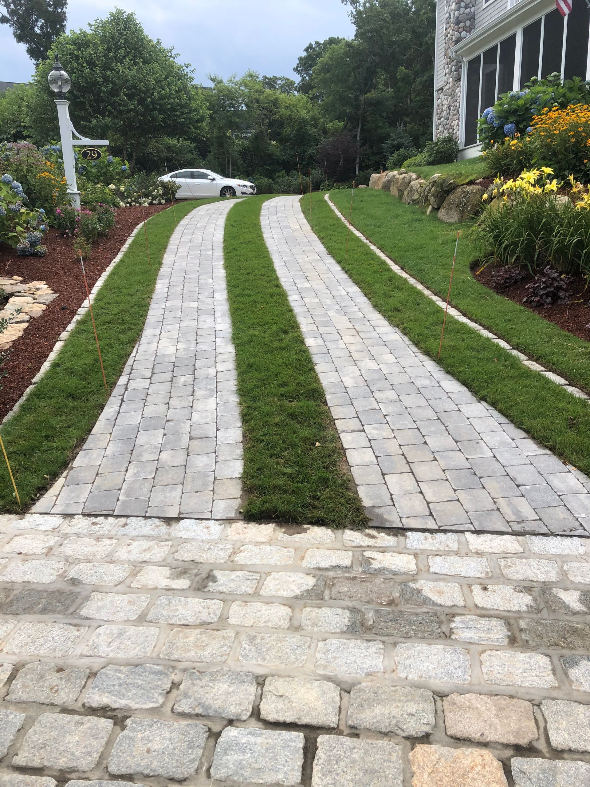 Brick driveway with a green grass center strip leading up a landscaped home entrance