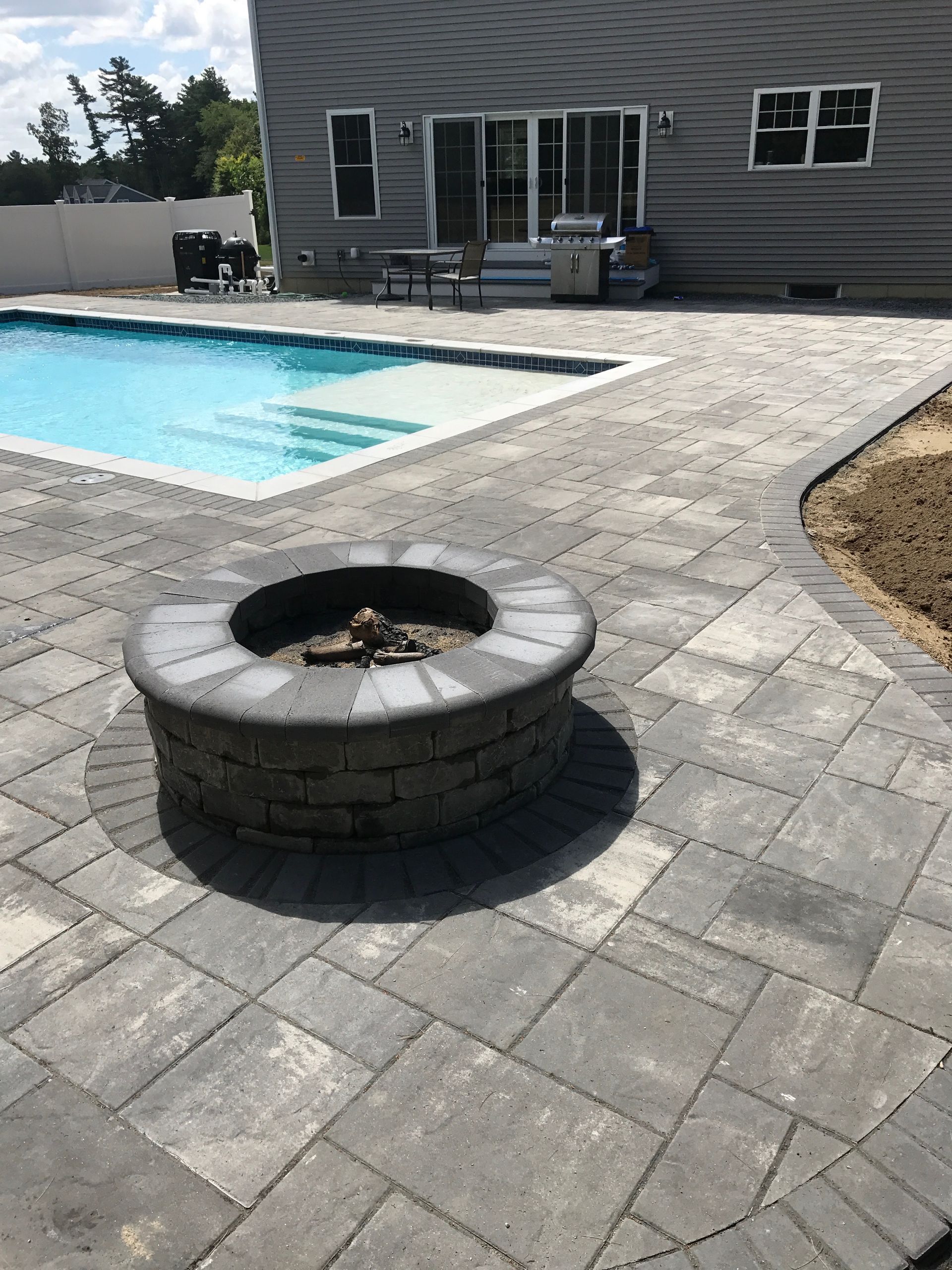 Backyard patio with a swimming pool, stone pavers, and a circular fire pit in the foreground