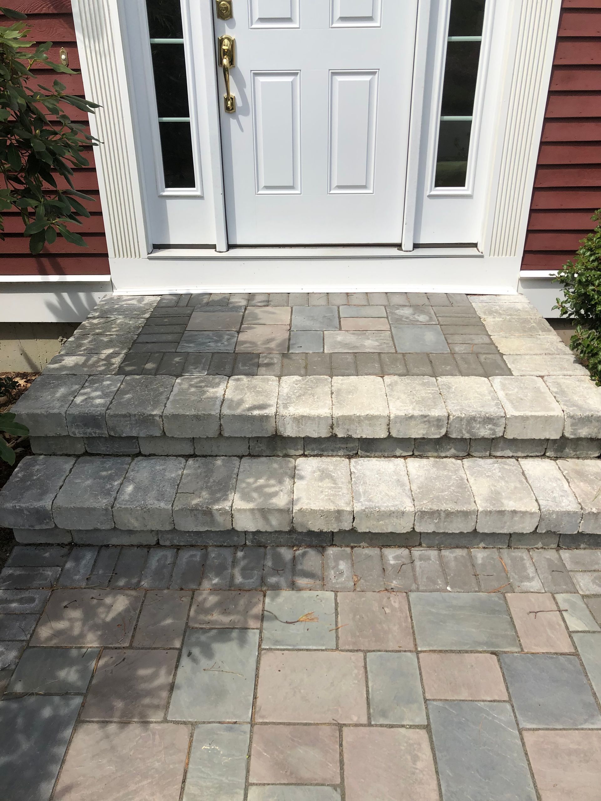 Front porch with white door and three stone steps leading up from a paved walkway